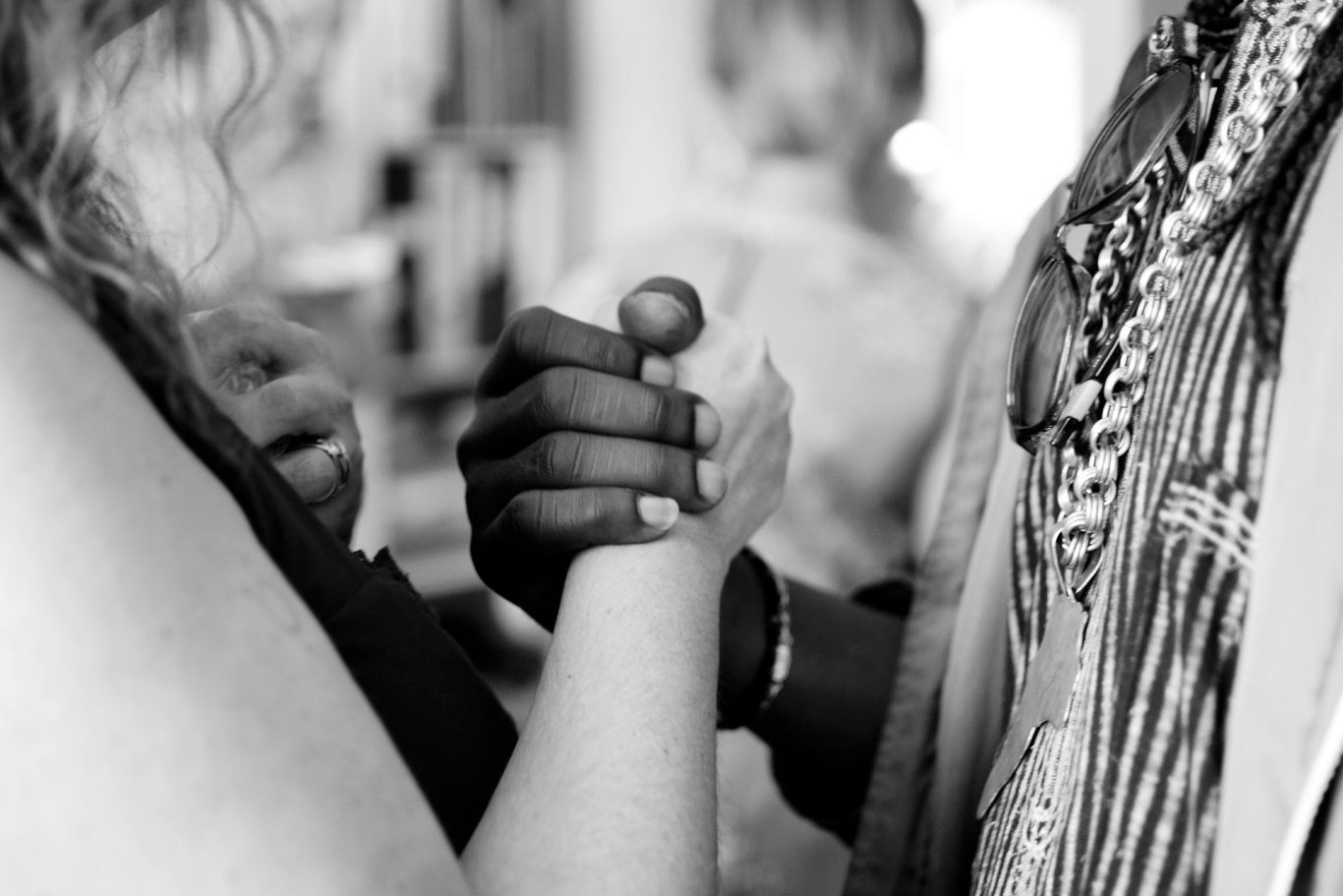 Two hands clasped together in a supportive gesture, one dark-skinned and one light-skinned.