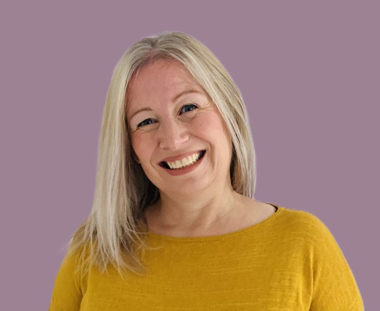 Smiling woman with long blonde hair wearing a yellow top against a purple background.